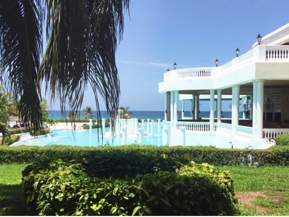 A large white house with a pool and lots of greenery.